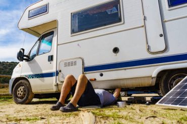 Man lying on ground, repairing bottom of the caravan vehicle.